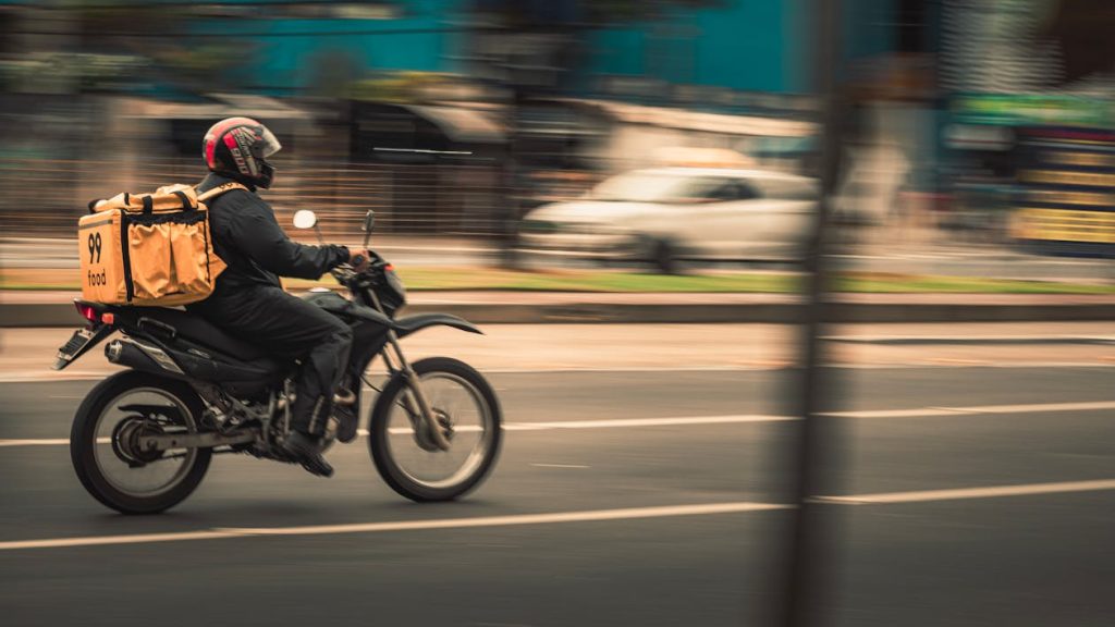 Food delivery motorcycle rider with delivery bag riding through Qatar city streets